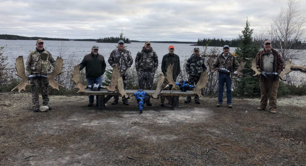 8 men standing in front of 6 moose racks