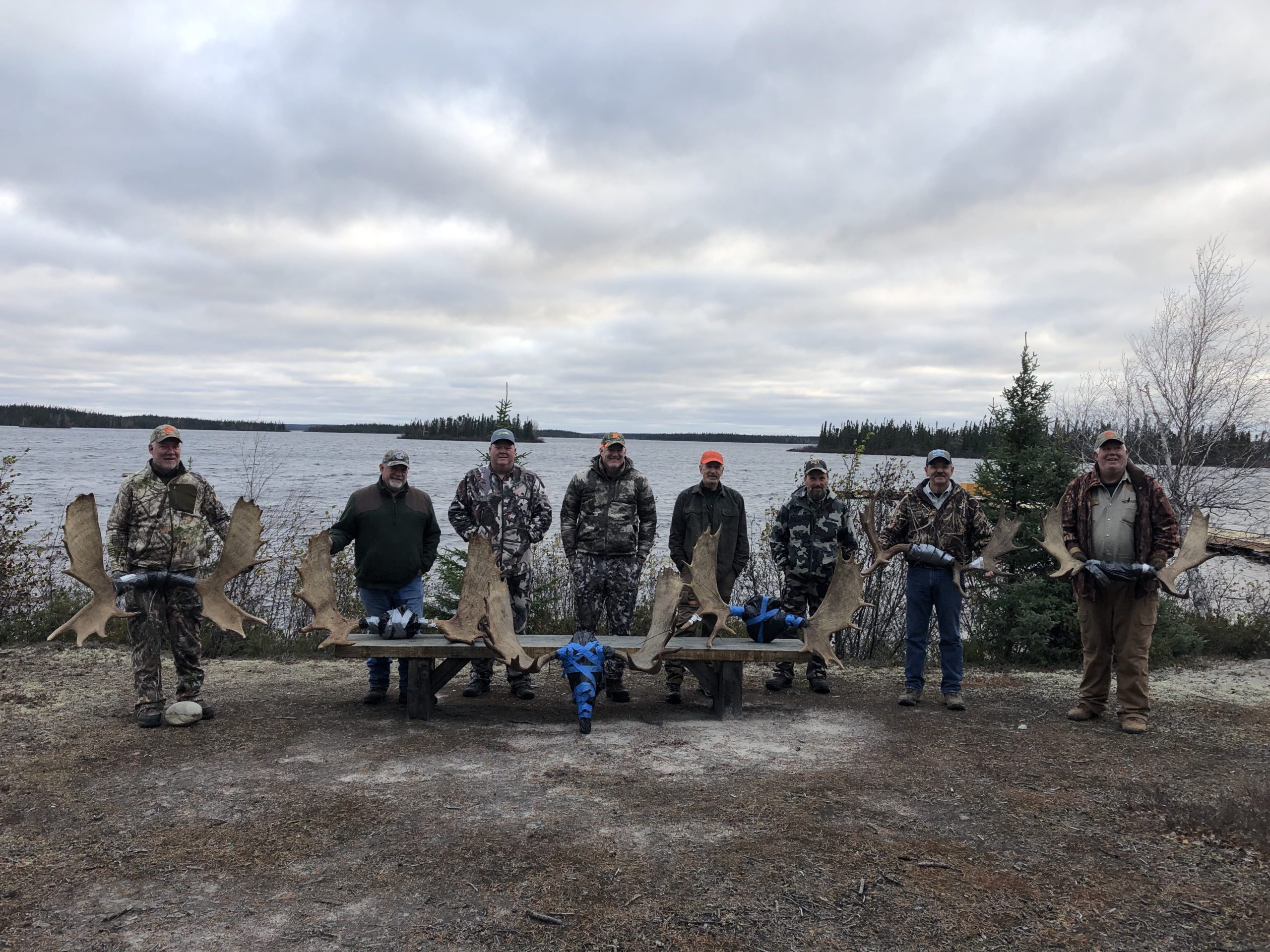 8 men standing in front of 6 moose racks