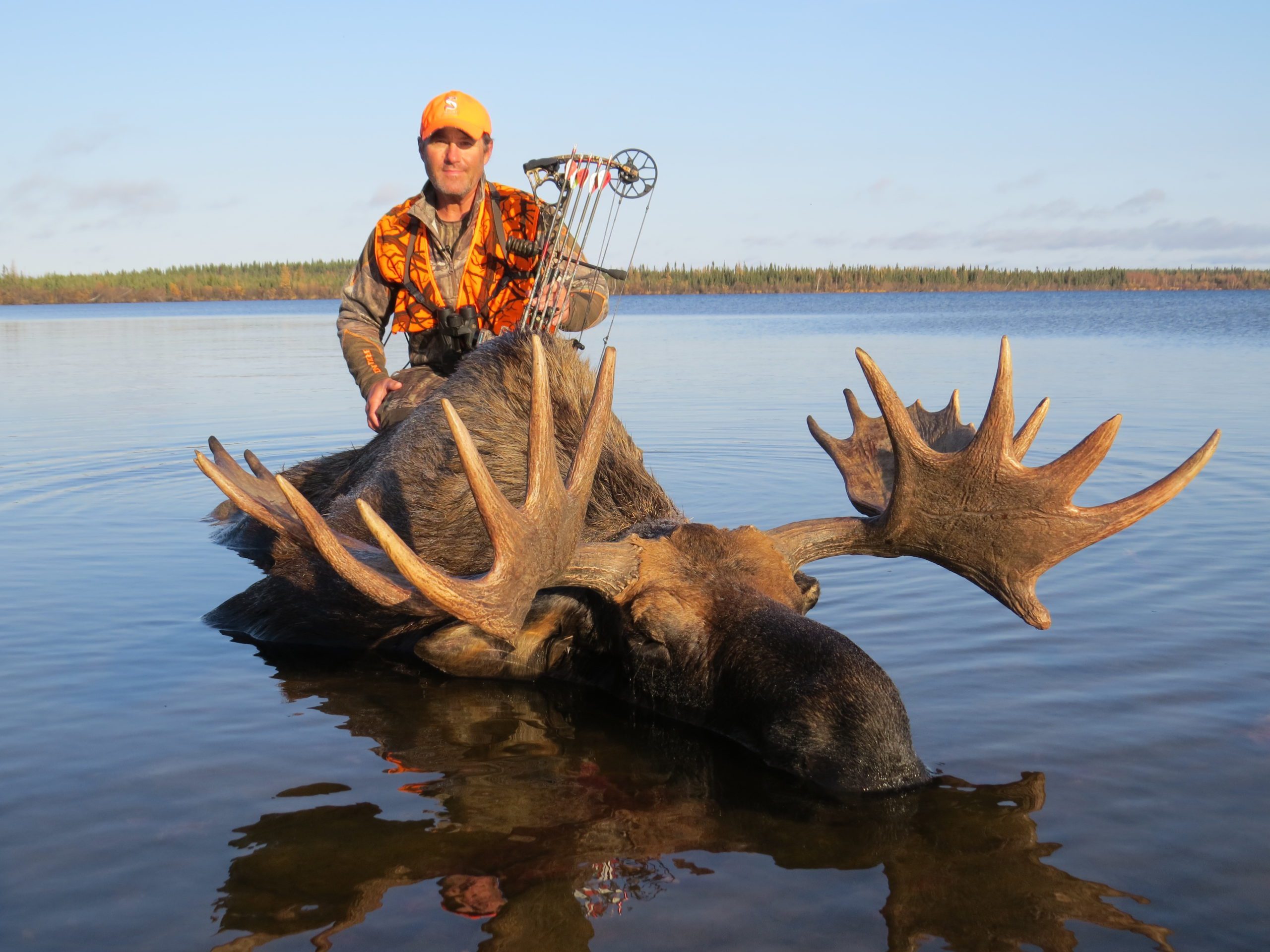 portrait of a man standing in water behind a freshly killed moose