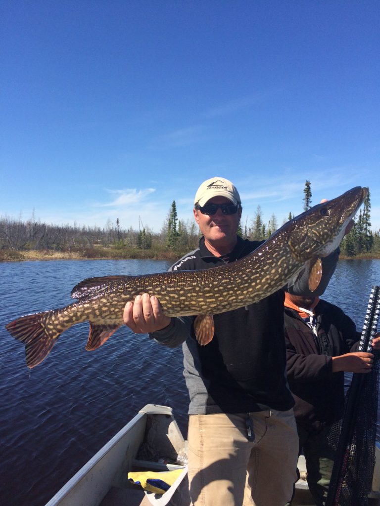 portrait of joe holding a large pike fish while standing in a boat on water