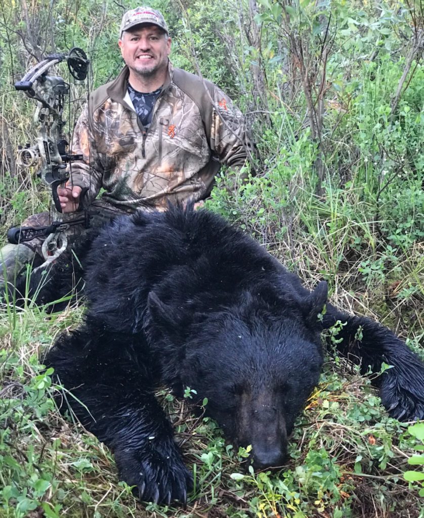 portrait of terry behind a dead black bear while holding a bow