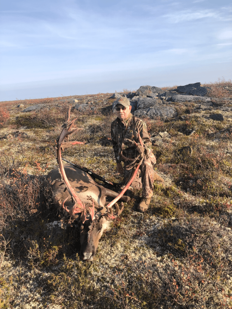 portrait of a man standing behind a freshly killed caribou