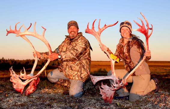 man and woman each kneeling and holding a skull of a caribou